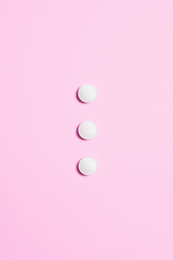 A minimalist composition featuring three white pills on a vibrant pink background.
