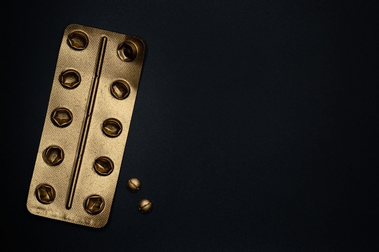 Golden blister pack and tablets on black for a healthcare concept visual.